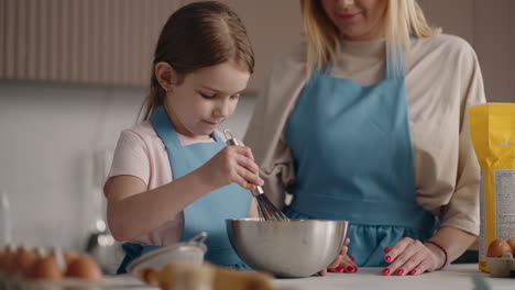 cute-little-girl-is-learning-to-cook-and-helping-to-parent-in-home-kitchen-mixing-dough-or-whipping-cream